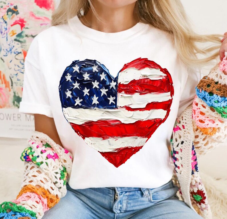 Pu&ograve; includere: Maglietta bianca con un design a forma di cuore dipinto a mano con i colori della bandiera americana. La bandiera &egrave; rossa, bianca e blu.