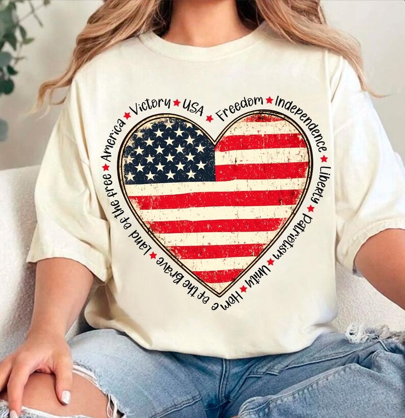 May include: A white t-shirt with a red, white, and blue heart-shaped American flag design. The words "Home of the Brave Land of the free America Victory * USA * Freedom * Independence * Liberty * Patriotism * Unity" are printed around the heart.
