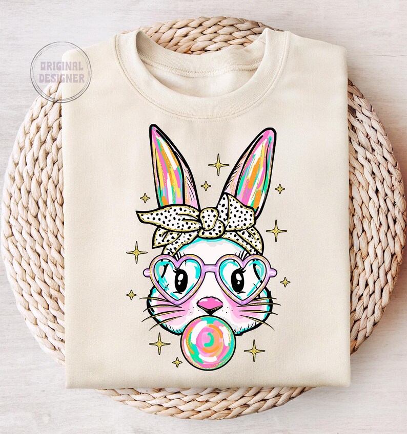 May include: A white sweatshirt with a colorful cartoon bunny wearing pink heart-shaped sunglasses and a black and white polka dot headband. The bunny is holding a colorful lollipop in its mouth.