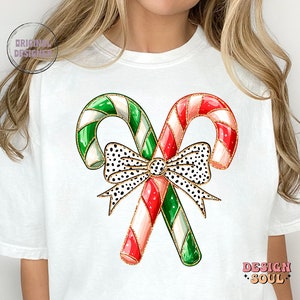 May include: White t-shirt with a graphic of two candy canes tied together with a black and white polka dot bow. The candy canes are red and white and green and white.