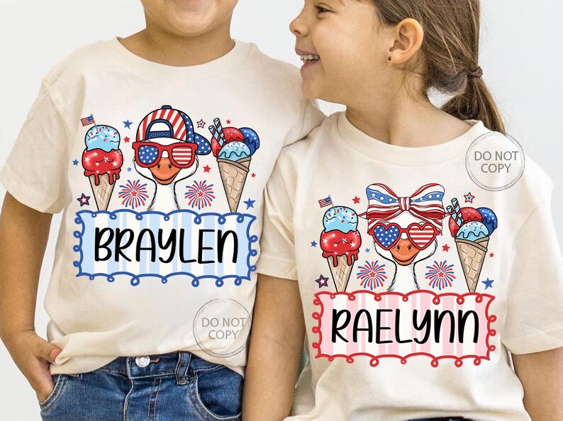 May include: Two children's t-shirts with patriotic ice cream cone designs. One shirt features the name "BRAYLEN" in blue, the other "RAELYNN" in red. Each shirt has a cartoon duck wearing sunglasses and a hat with a red, white, and blue theme.