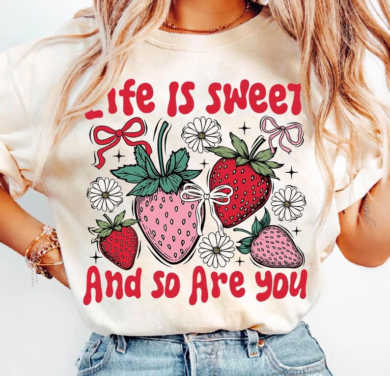 May include: A white t-shirt with a graphic design of strawberries and flowers. The text "Life is sweet and so are you" is printed in red on the shirt.