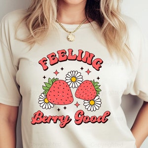 May include: White t-shirt with a graphic design of two strawberries and the text "Feeling Berry Good" in a retro font.