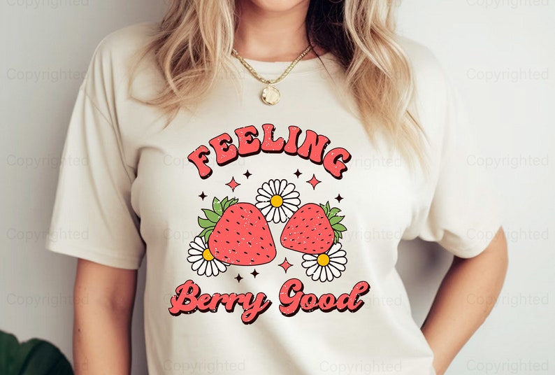 May include: White t-shirt with a graphic design of two strawberries and the text "Feeling Berry Good" in a retro font.