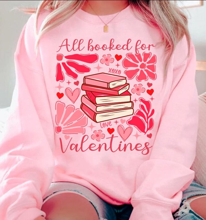 May include: Pink sweatshirt with a graphic design of a stack of books, hearts, flowers, and the text "All booked for Valentines".