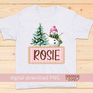 May include: White t-shirt with a pink and white gingham design featuring a snowman and a Christmas tree with the name "Rosie" on it.
