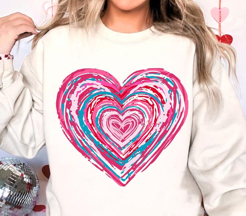 Pu&ograve; includere: Una felpa bianca con un grande disegno a forma di cuore rosa, rosso e blu. Il cuore &egrave; composto da cerchi concentrici di colore.