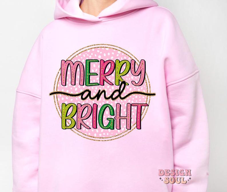 May include: A light pink hoodie with the words "MERRY and BRIGHT" in a colorful, playful font. The text is set within a pink circle with white polka dots and a gold glitter border. The hoodie has a drawstring hood.