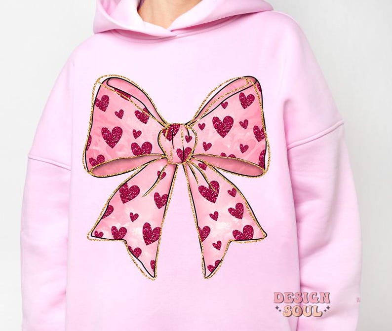 May include: Pink hoodie with a large, gold glitter bow with pink hearts. The bow is centered on the front of the hoodie.