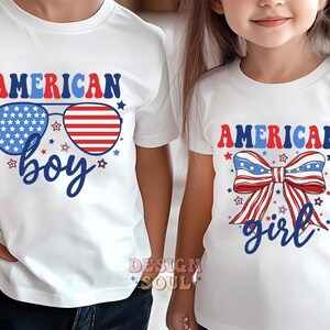 May include: Two white t-shirts with red, white, and blue American flag designs. The boy's shirt says "American Boy" with sunglasses featuring the American flag. The girl's shirt says "American Girl" with a red, white, and blue bow.