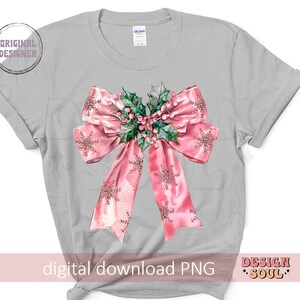May include: A gray t-shirt with a pink bow with a green holly and red berry design. The bow has a snowflake pattern.