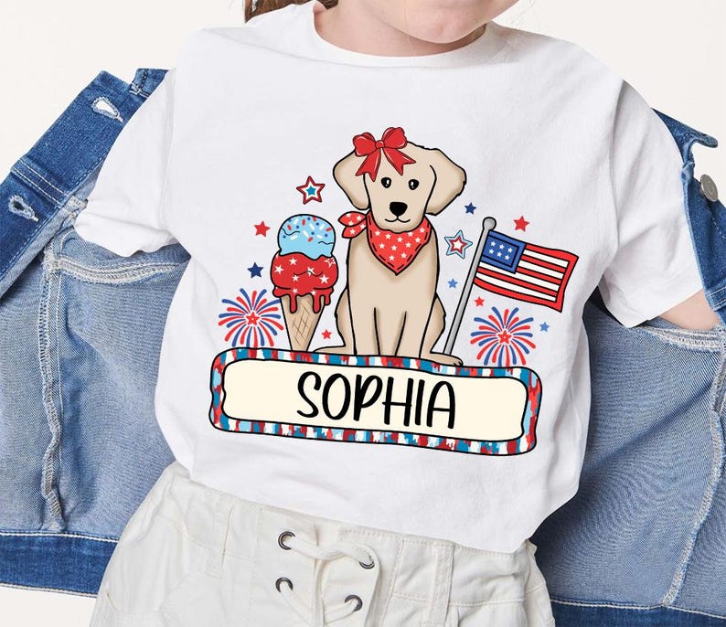 Pu&ograve; includere: Maglietta bianca con un design patriottico rosso, bianco e blu con un cane, un cono gelato e fuochi d'artificio. Il testo "Sophia" &egrave; stampato sulla maglietta.