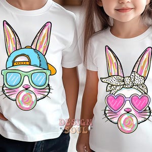 May include: Two white t-shirts with a colorful cartoon bunny wearing sunglasses and a hat on one shirt and a colorful cartoon bunny wearing heart-shaped sunglasses and a bandana on the other shirt.