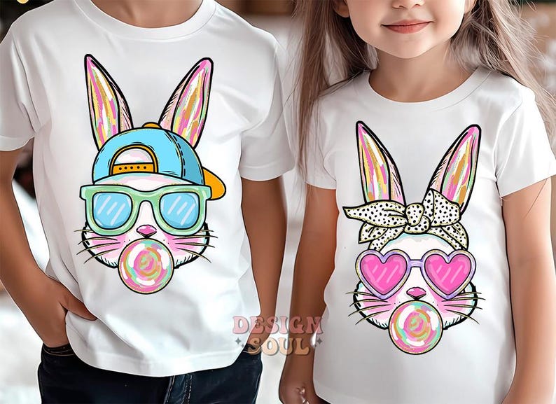 May include: Two white t-shirts with a colorful cartoon bunny wearing sunglasses and a hat on one shirt and a colorful cartoon bunny wearing heart-shaped sunglasses and a bandana on the other shirt.