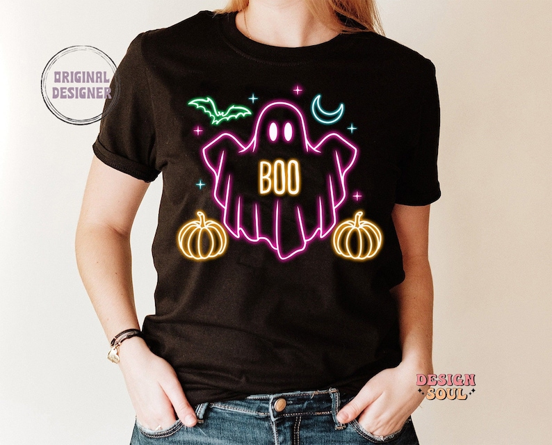 May include: Black t-shirt with a neon pink ghost graphic and the word "BOO" in neon yellow. The ghost is surrounded by neon green bats, yellow moons, and orange pumpkins.