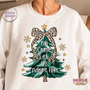 May include: White sweatshirt with a green Christmas tree design. The tree has a leopard print bow and the text "Oh Come Let Us Adore Him".
