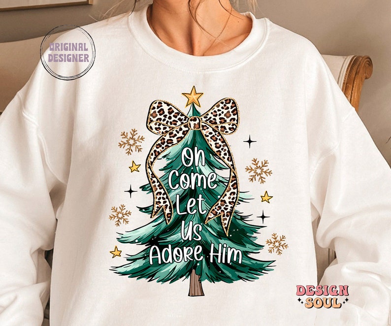 May include: White sweatshirt with a green Christmas tree design. The tree has a leopard print bow and the text "Oh Come Let Us Adore Him".