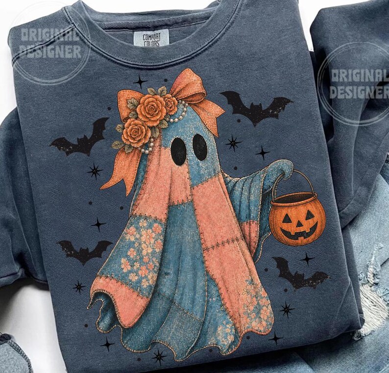 May include: A blue sweatshirt featuring a patchwork ghost design with a pumpkin bucket. The ghost has a bow, floral accents, and black eyes. Bats and stars are scattered around the ghost, creating a Halloween theme.