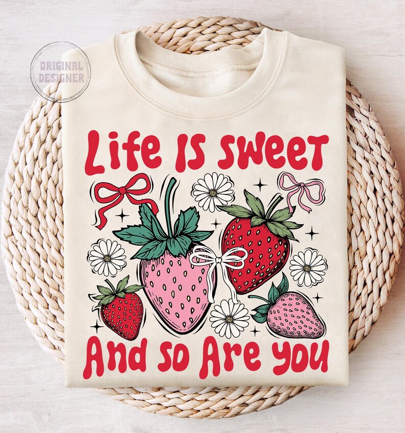 May include: A cream-colored sweatshirt with the text "Life is sweet and so are you" in red. The design features strawberries, flowers, and bows.