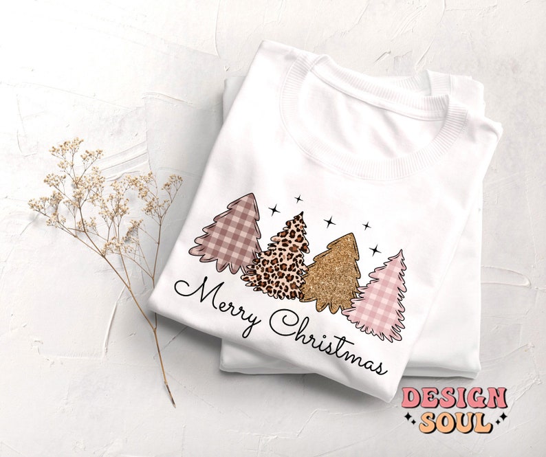 May include: White sweatshirt with a pink, brown, and gold Christmas tree design. The text "Merry Christmas" is written in black cursive below the trees.