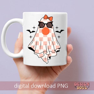 May include: A white ceramic mug with a pink and white checkered ghost wearing black sunglasses and a pink bow. The ghost has a red nose and is surrounded by black bats and stars.