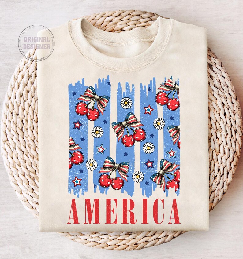 May include: A cream-colored sweatshirt with a blue and white striped design featuring red cherries and stars. The word "AMERICA" is printed in red at the bottom of the shirt.