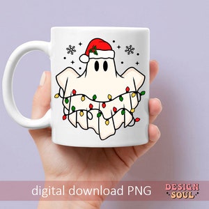May include: White ceramic mug with a ghost wearing a Santa hat and surrounded by Christmas lights. The mug has a black handle and a white background.