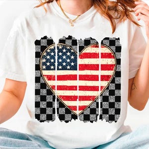 May include: White t-shirt with a distressed American flag heart design. The heart is surrounded by a checkered pattern.