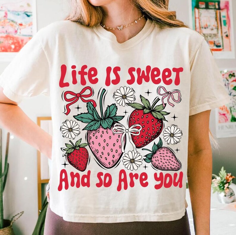 May include: A white t-shirt with a graphic design of strawberries, flowers, and the text "Life is sweet and so are you".