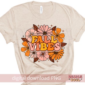 May include: A beige t-shirt featuring a graphic design of autumn-coloured flowers and the text "Fall Vibes" in a retro font.