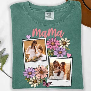 May include: A teal Comfort Colors t-shirt featuring the word "Mama" in pink script. The shirt is decorated with two polaroid-style photos of a mother and child, surrounded by pink, purple, and white flowers, and a pink butterfly.