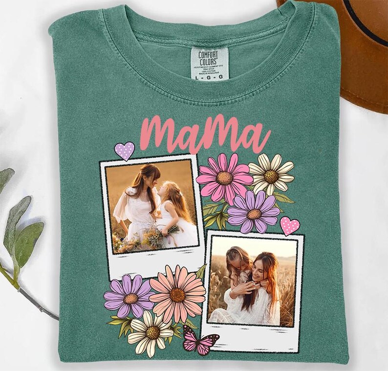 May include: A teal Comfort Colors t-shirt featuring the word "Mama" in pink script. The shirt is decorated with two polaroid-style photos of a mother and child, surrounded by pink, purple, and white flowers, and a pink butterfly.