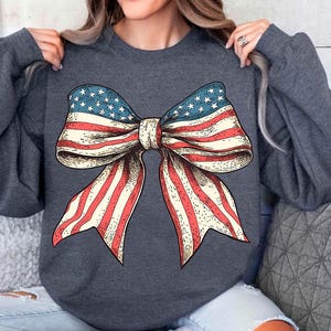 Peut inclure: Un sweat-shirt gris fonc&eacute; avec un grand n&oelig;ud rouge, blanc et bleu imprim&eacute; sur le devant. Le n&oelig;ud est dans le style du drapeau am&eacute;ricain.