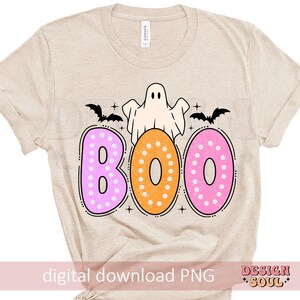 Op de afbeelding: Een beige T-shirt met een spook en het woord "BOO" in roze, oranje en witte stippen. De letters zijn donutvormig.