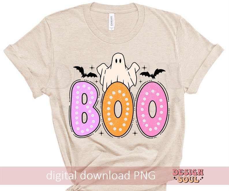 Op de afbeelding: Een beige T-shirt met een spook en het woord "BOO" in roze, oranje en witte stippen. De letters zijn donutvormig.
