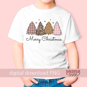May include: A white t-shirt with a pink, brown, and gold Christmas tree design. The trees are decorated with plaid, leopard print, and glitter. The text "Merry Christmas" is printed below the trees.