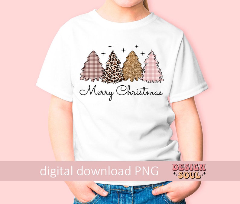 May include: A white t-shirt with a pink, brown, and gold Christmas tree design. The trees are decorated with plaid, leopard print, and glitter. The text "Merry Christmas" is printed below the trees.