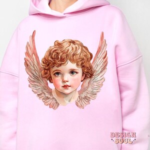 Op de afbeelding: Een roze hoodie met een afbeelding van een cherubijn met vleugels. De cherubijn heeft blond haar en blauwe ogen. De hoodie heeft de tekst "DESIGN SOUL" gedrukt in de rechterbenedenhoek.