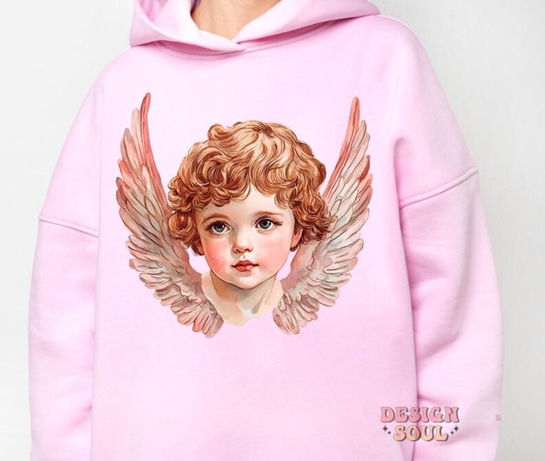 Op de afbeelding: Een roze hoodie met een afbeelding van een cherubijn met vleugels. De cherubijn heeft blond haar en blauwe ogen. De hoodie heeft de tekst "DESIGN SOUL" gedrukt in de rechterbenedenhoek.