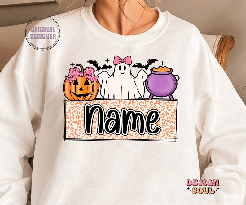 May include: White sweatshirt with a Halloween-themed design featuring a ghost, a pumpkin, and a cauldron. The design is on a leopard print background with the word "name" in black text.