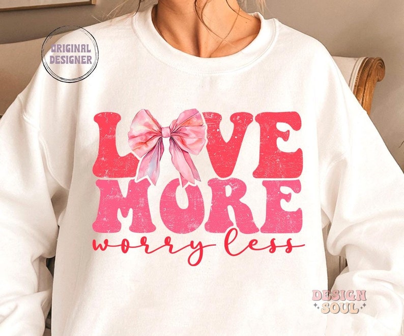 May include: White sweatshirt with a pink bow and the text "LOVE MORE worry less" in pink and red letters.
