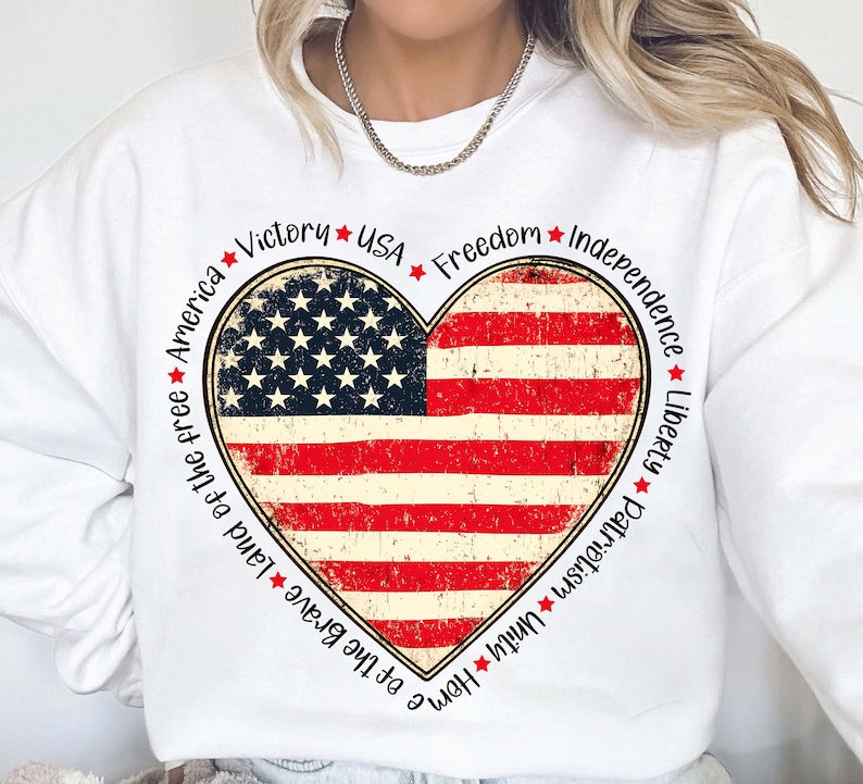 May include: White sweatshirt with a red, white, and blue heart-shaped American flag design. The heart is surrounded by the words "Home of the Brave, Land of the Free, America, Victory, USA, Freedom, Independence, Liberty, Patriotism, Unity".