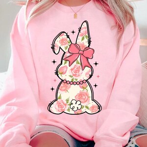 May include: Pink sweatshirt with a floral bunny graphic. The bunny has a pink bow and is surrounded by stars.