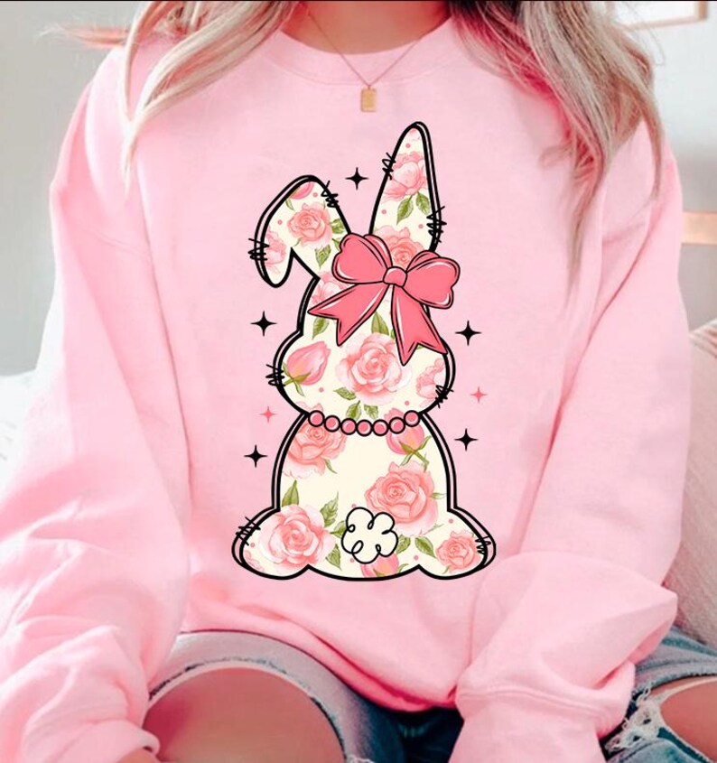 May include: Pink sweatshirt with a floral bunny graphic. The bunny has a pink bow and is surrounded by stars.