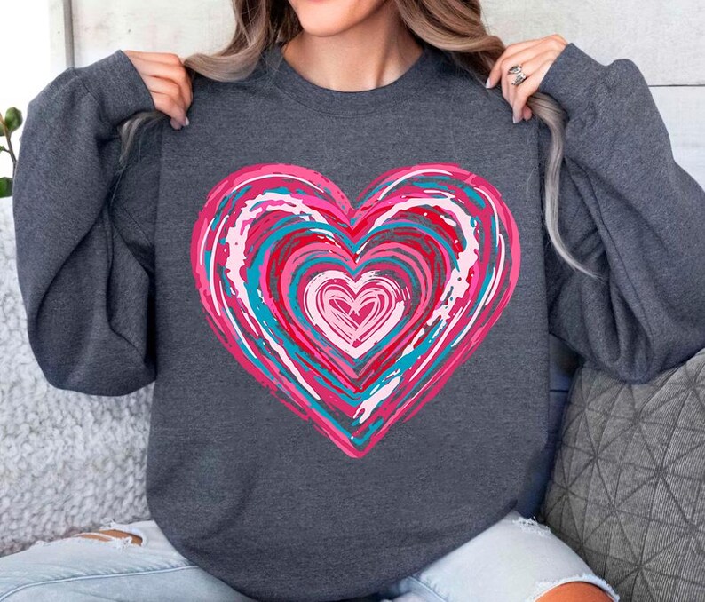 Pu&ograve; includere: Una felpa grigia scura con un grande disegno a forma di cuore rosa, blu e bianco. Il cuore &egrave; composto da cerchi concentrici di vernice.