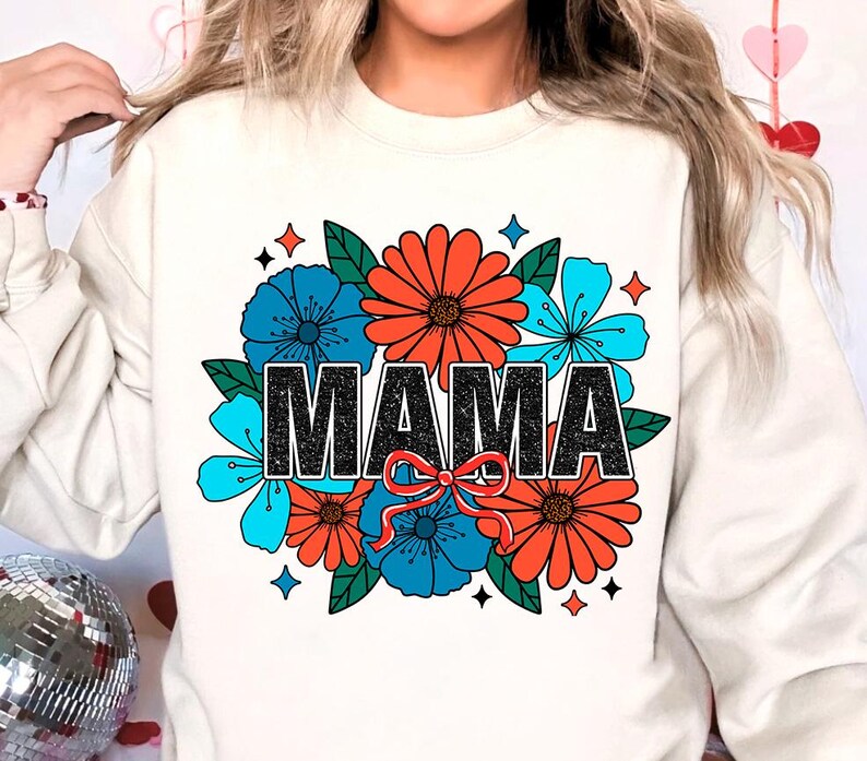 Pu&ograve; includere: Felpa bianca con un design floreale e la parola "MAMA" in lettere glitter nere. I fiori sono rossi, blu e verdi.