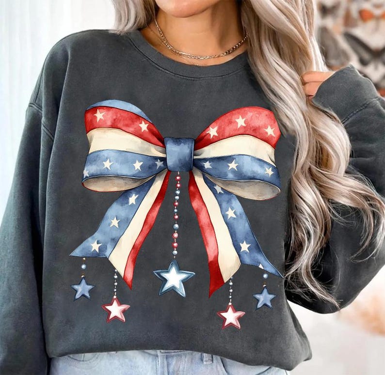 May include: A charcoal gray sweatshirt with a large red, white, and blue bow with stars printed on it. The bow has a blue center and is accented with dangling stars.