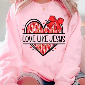 May include: Pink sweatshirt with a red and gold heart design and the text "LOVE LIKE JESUS".