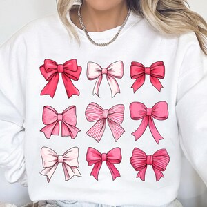 May include: White sweatshirt with a pink and white bow pattern. The bows are arranged in a grid of nine.