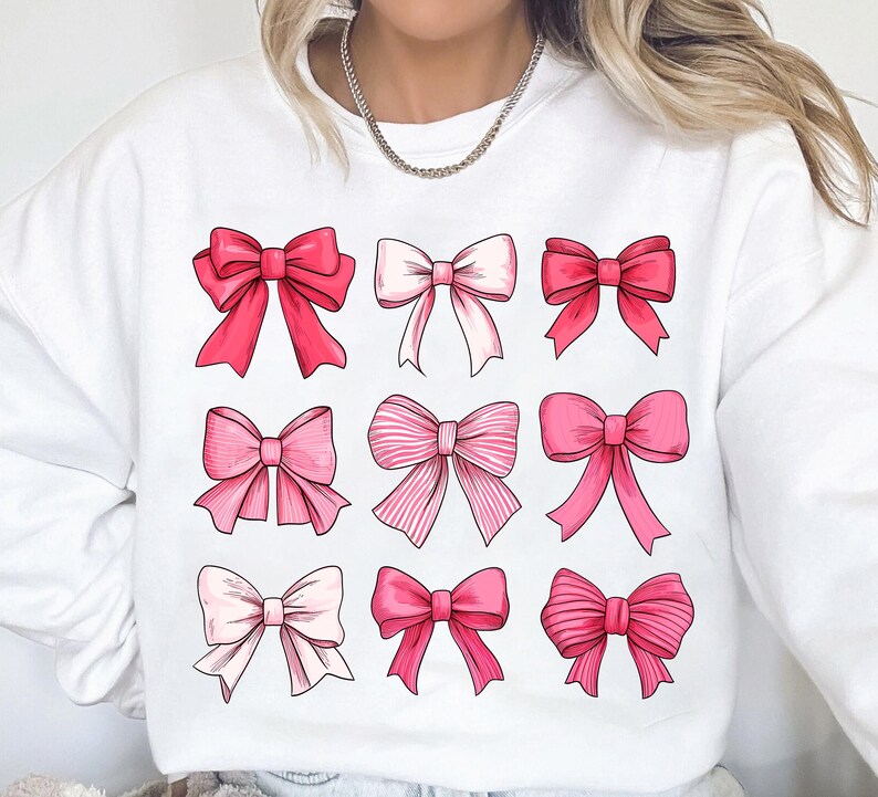 May include: White sweatshirt with a pink and white bow pattern. The bows are arranged in a grid of nine.